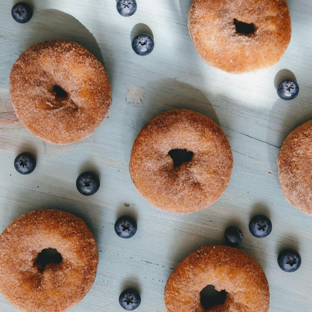 Cinnamon-sugar doughnuts arranged with scattered blueberries on a pale blue wooden board