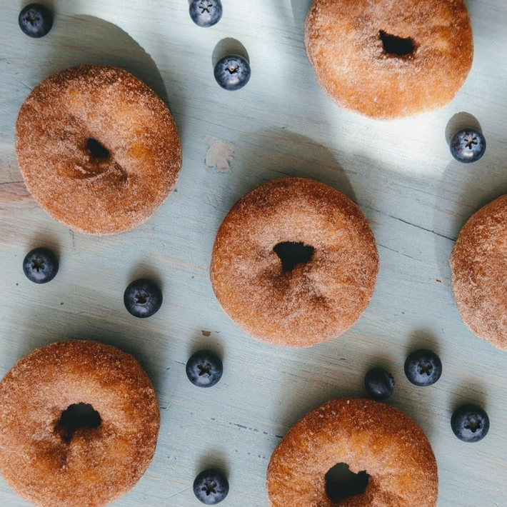 Cinnamon-sugar doughnuts arranged with scattered blueberries on a pale blue wooden board