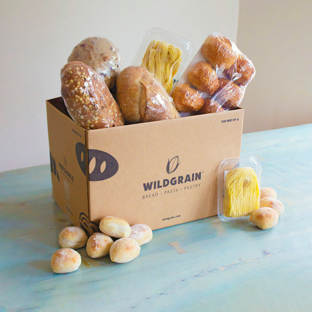 A box of assorted breads and pasta from Wildgrain, with rolls and packaged items visible.