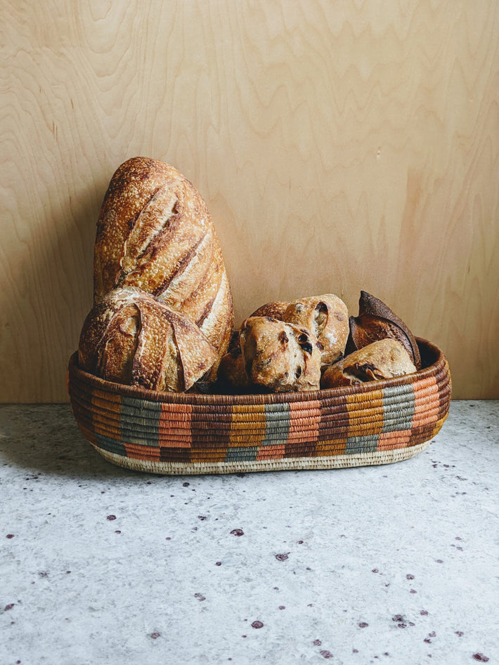 A variety of artisanal breads in a woven basket, including a large loaf and smaller rolls.