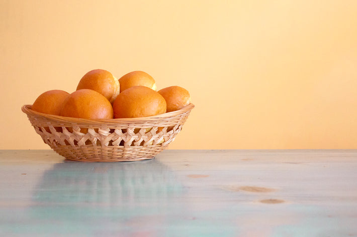 A woven basket filled with oranges on a wooden table against a yellow background.