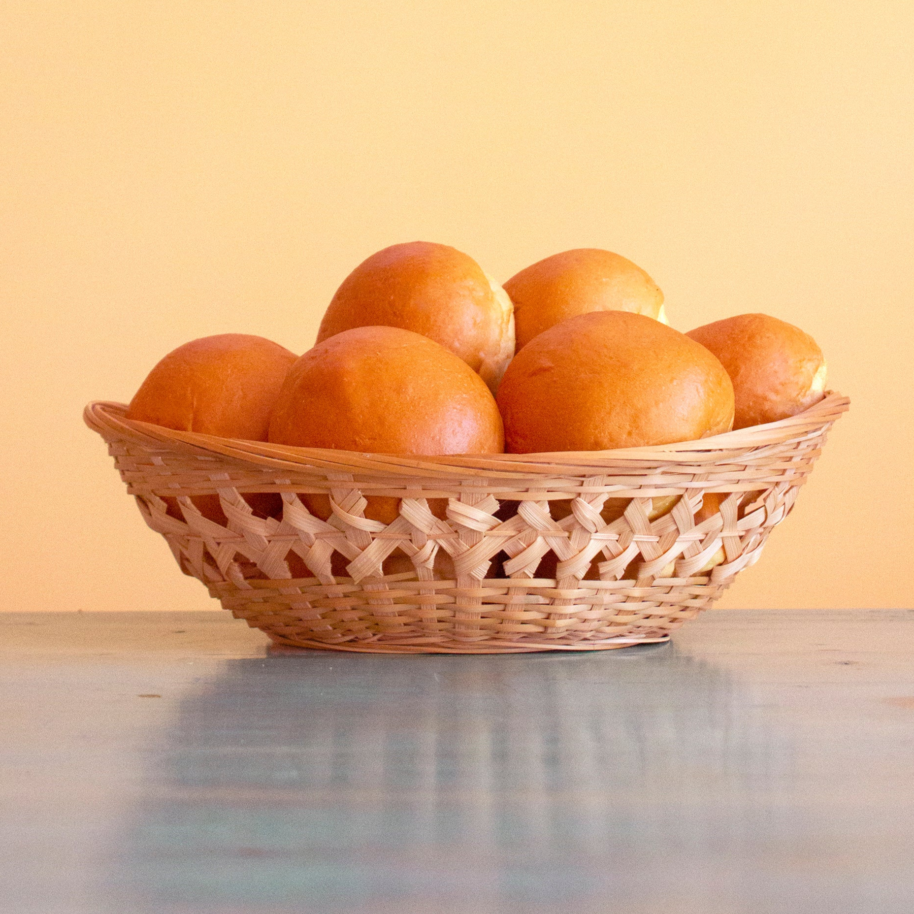 Woven basket of golden dinner rolls on a wooden table with warm yellow background