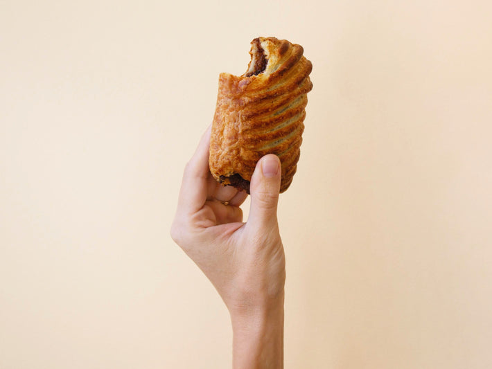 A hand holding a Chocolate Avalanche Croissant, showcasing its flaky texture.