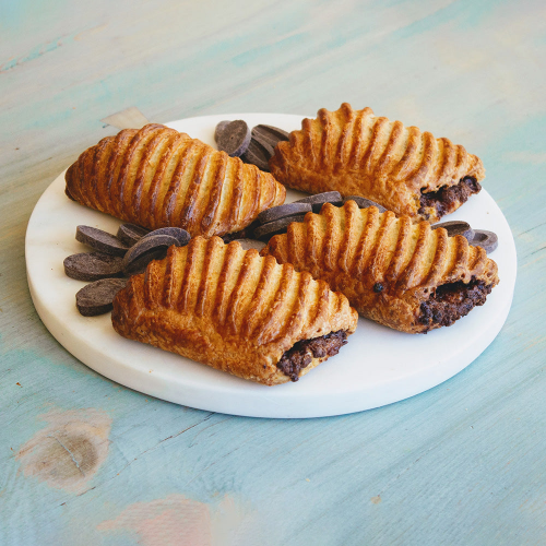 Four chocolate-filled puff pastries on a round white marble board with chocolate discs