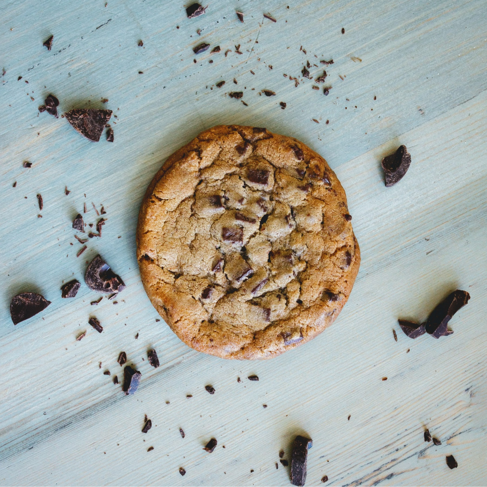 Chocolate chip cookie centered on light blue wooden surface with scattered chocolate chunks and crumbs.