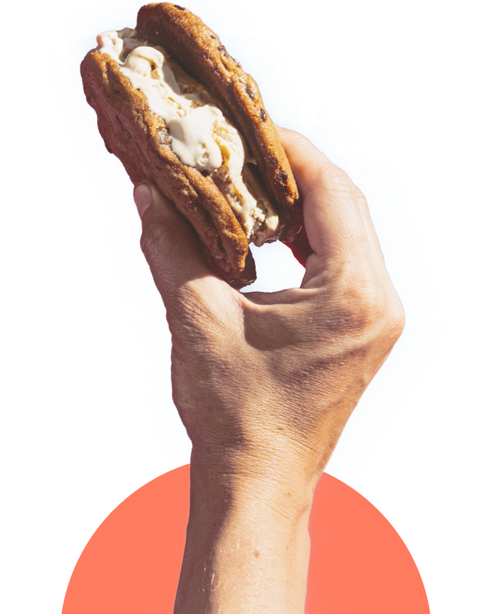 Gluten-Free Giant Chocolate Chunk Cookie Sandwich filled with ice cream, held in a hand against a colorful background.