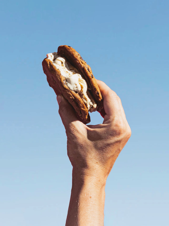 A hand holding a cookie sandwich against a blue sky background
