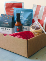 Angled view of Summer Treat Box with red tissue, granola pouch, caramels box, hot sauce bottle, and wrapped linzer cookies