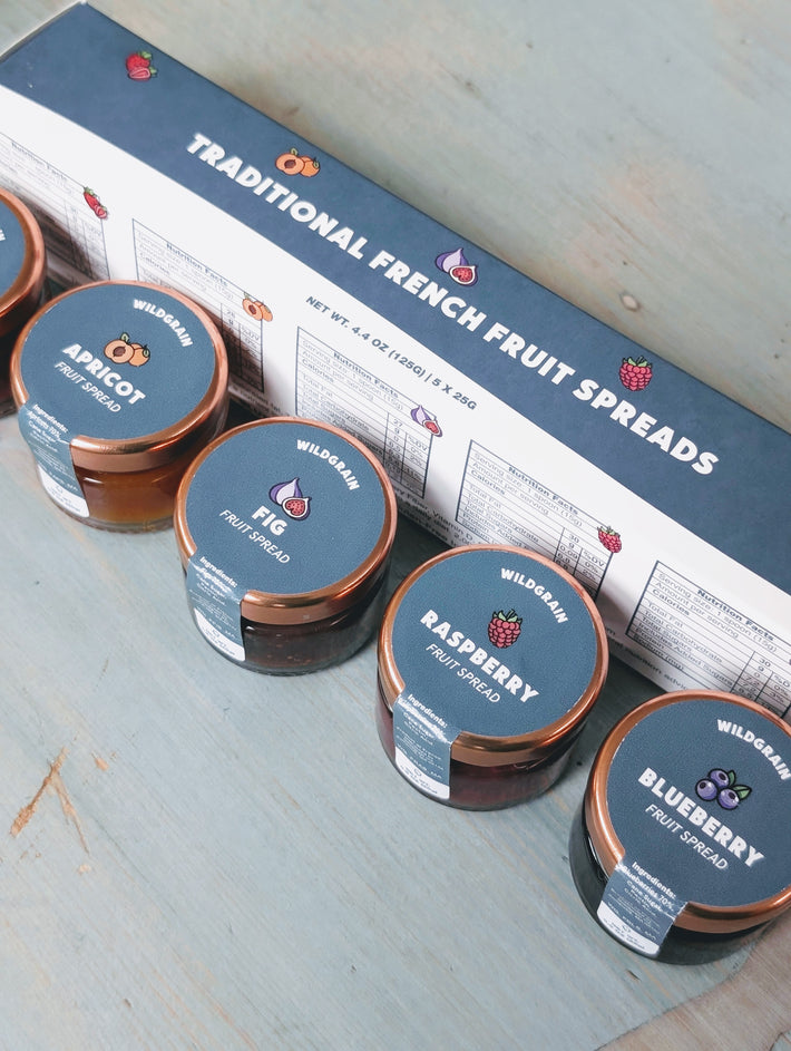 Angled view of Traditional French Fruit Spreads five-pack sampler with labeled jars and box on a blue wooden table