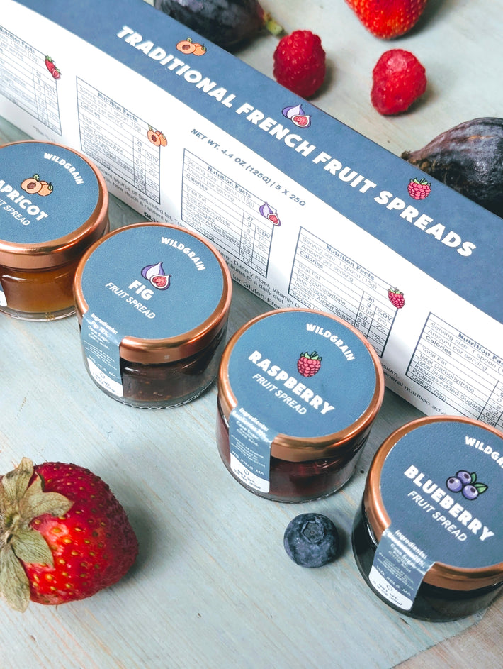 Angled view of Traditional French Fruit Spreads 5-pack sampler with apricot, fig, raspberry, and blueberry jars on blue tabletop