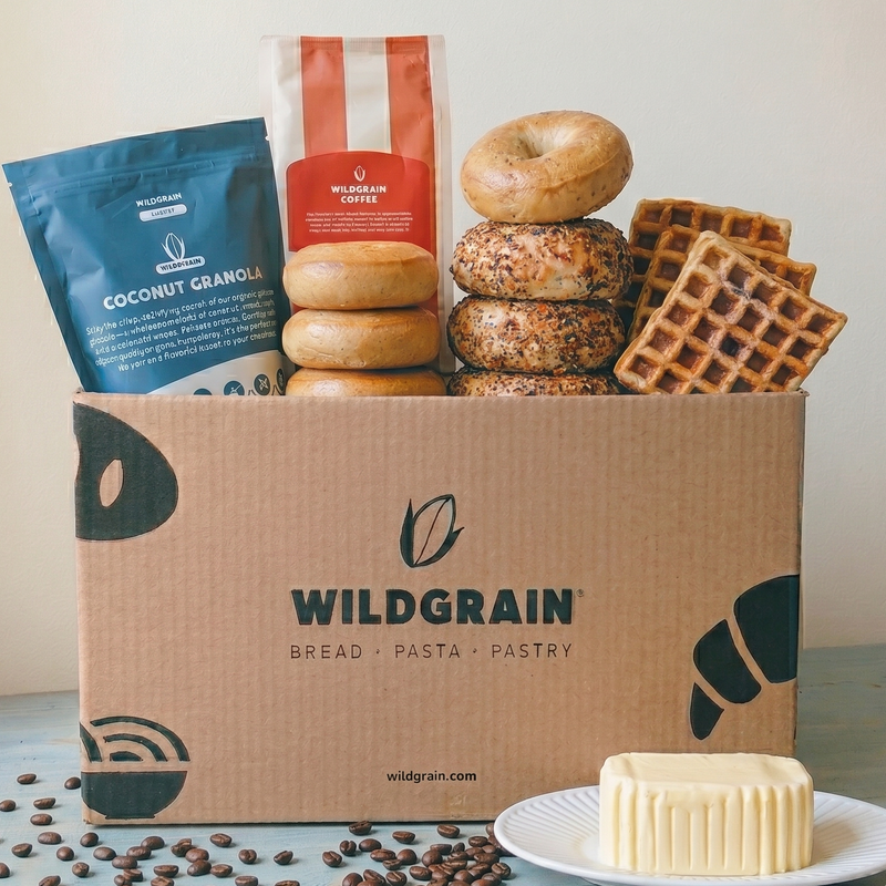 Front view of Wildgrain gluten-free breakfast box with stacked bagels, waffles, granola pouch, coffee bag, and butter
