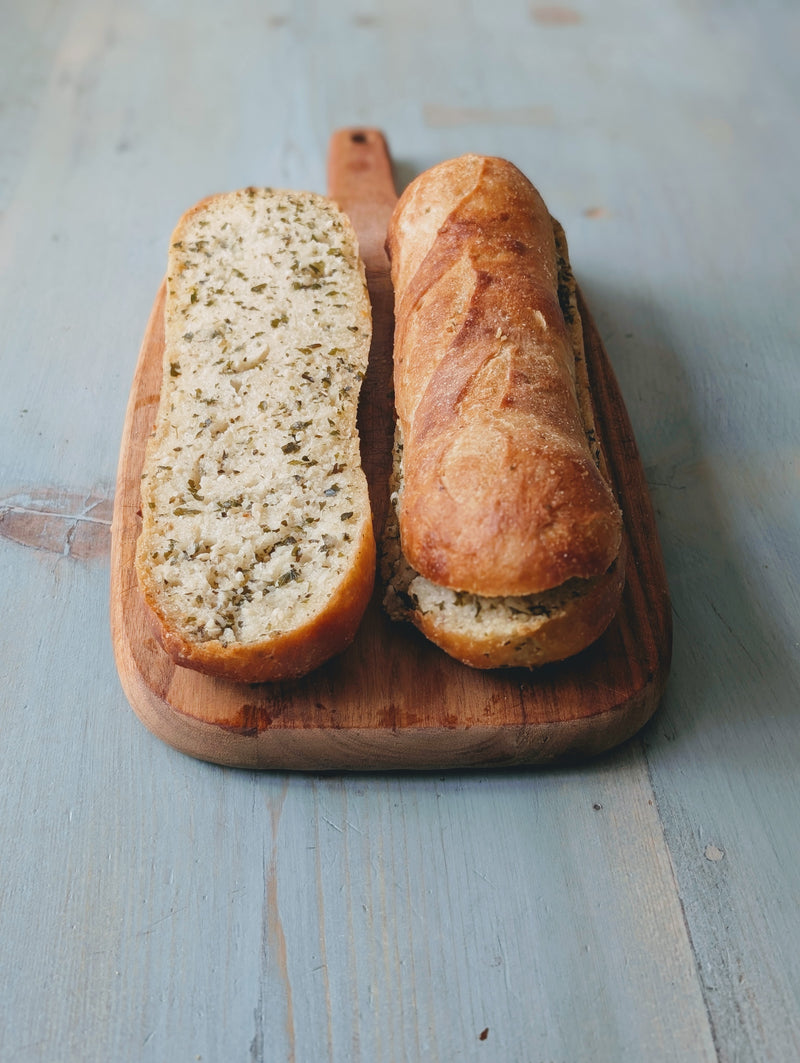 Overhead view of garlic butter baguette split open showcasing herbed garlic butter on a wooden board with light blue table