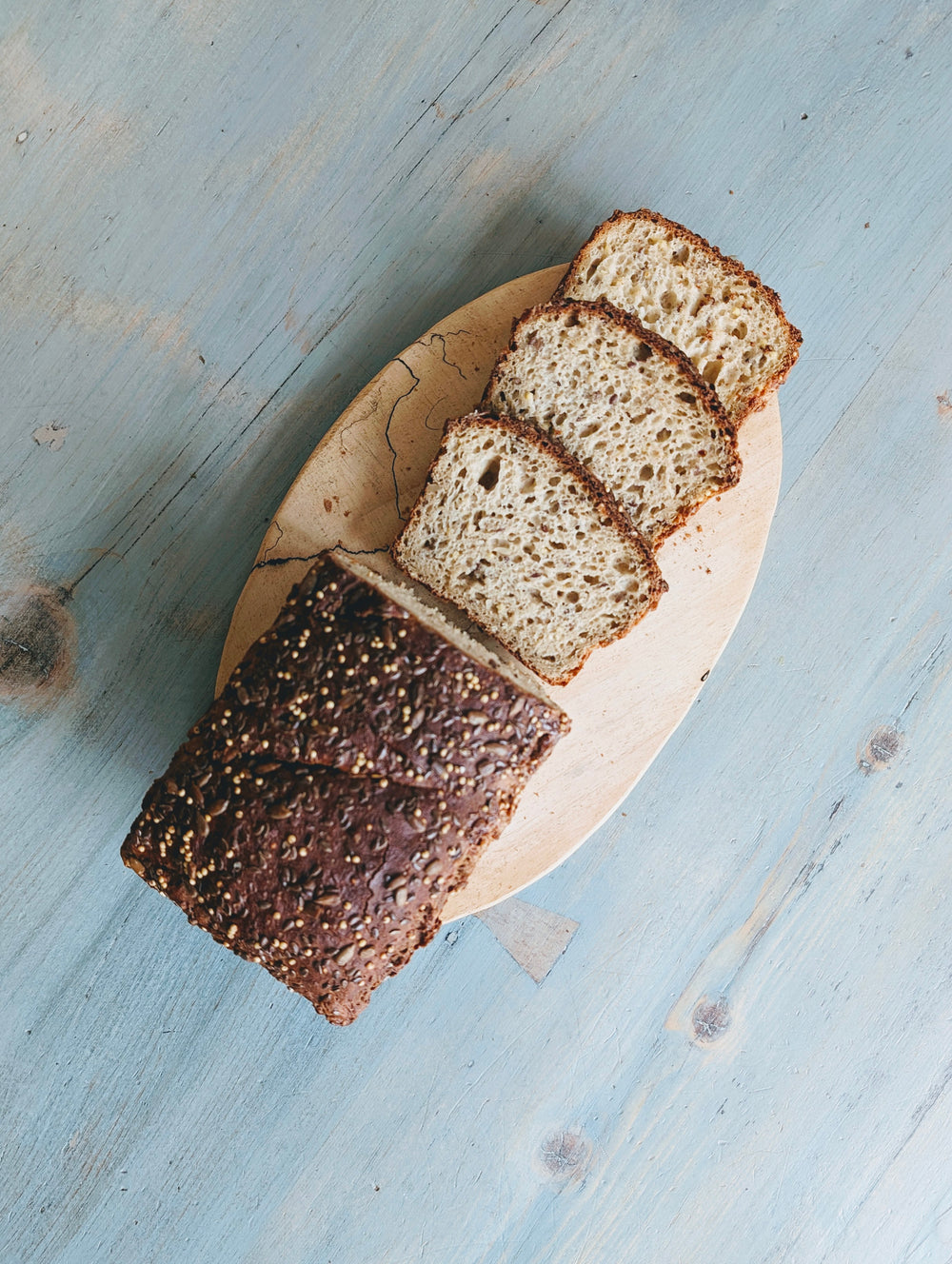 Sliced seeded loaf on a wooden board atop a distressed pale-blue table.
