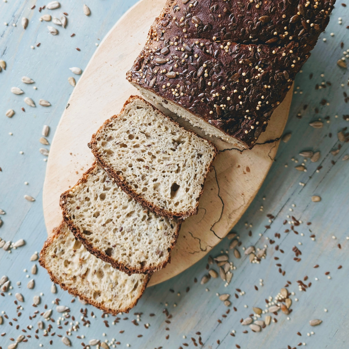 Gluten-Free Slow-Fermented Seeded Loaf sliced on a wooden board with scattered seeds.
