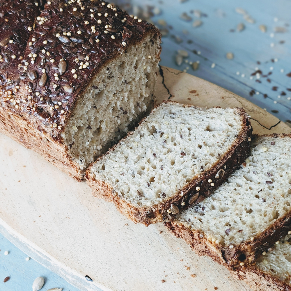 Sliced gluten-free slow-fermented seeded loaf on a wooden board, showcasing its texture and seeds.