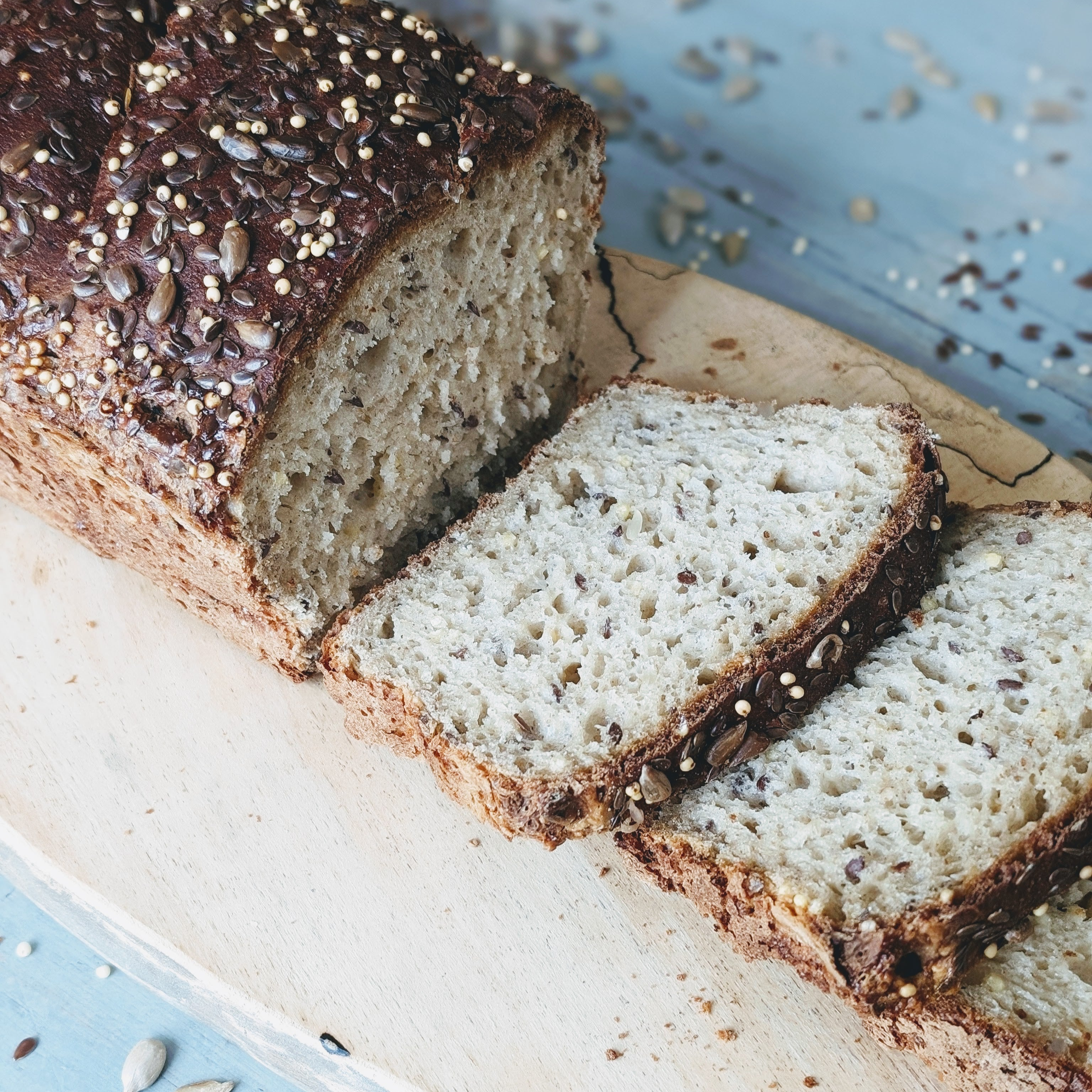 Sliced gluten-free slow-fermented seeded loaf on a wooden board, showcasing its texture and seeds.