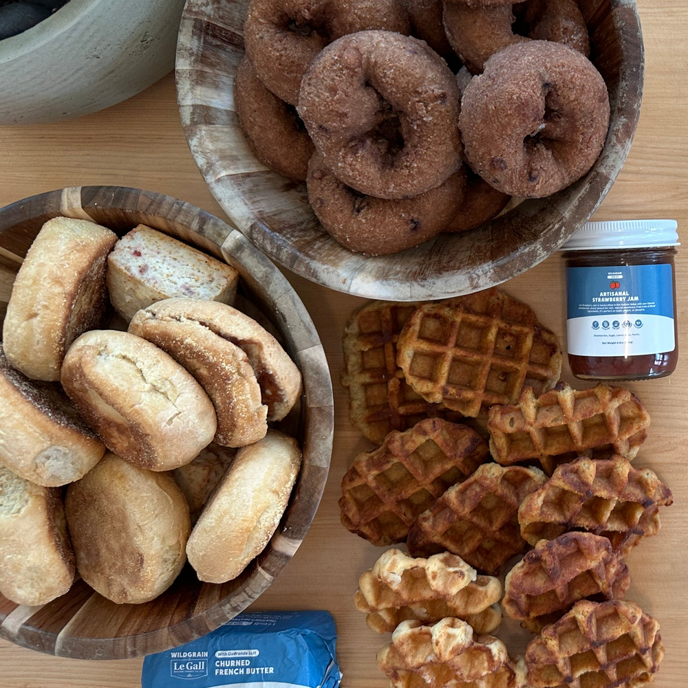 Top-down of Heat and Serve Catering Box: donuts, English muffins, maple waffles, jar of strawberry jam, and butter on wood