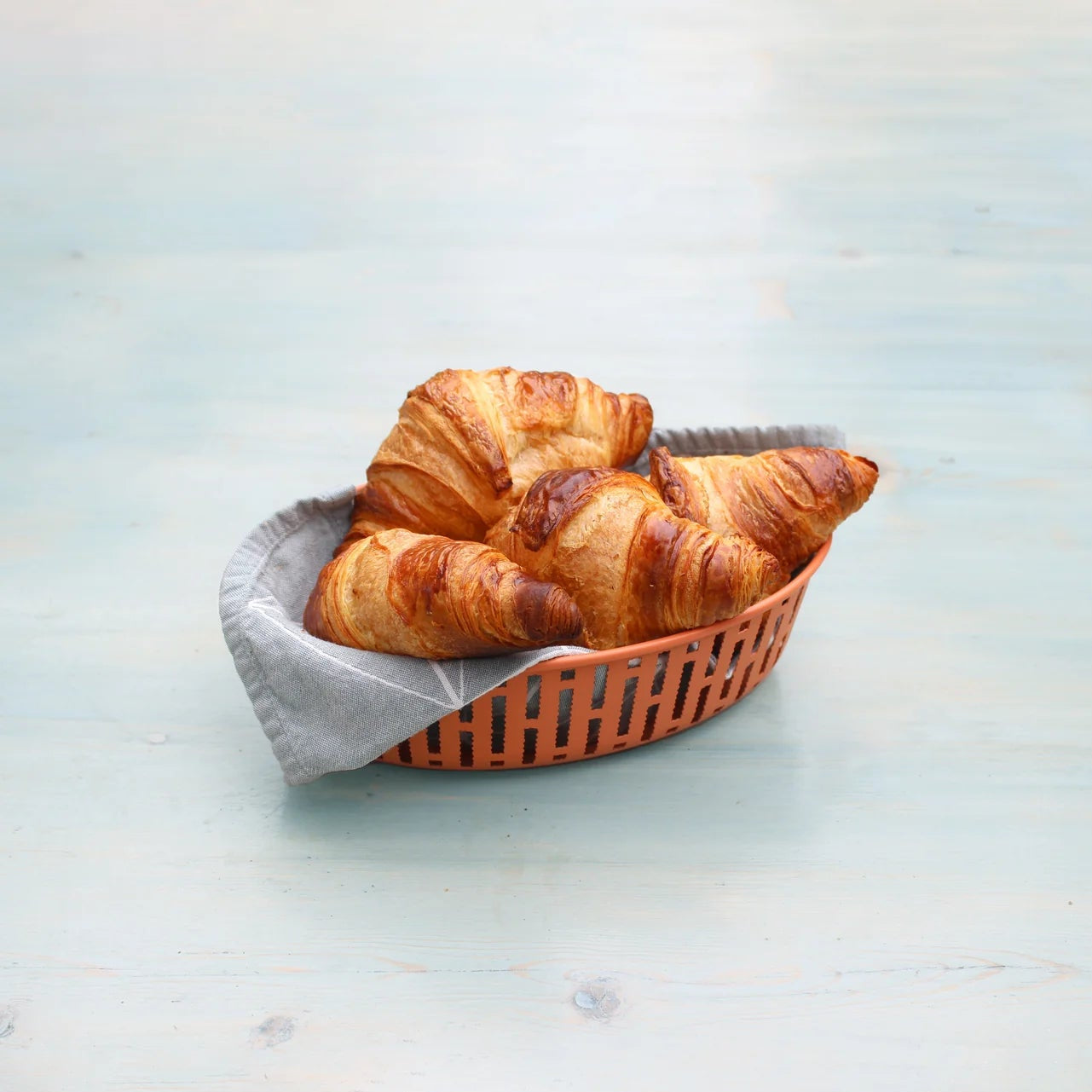 Three croissants in a brown basket on a light blue surface
