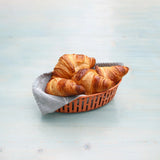 Three croissants in a brown basket on a light blue surface
