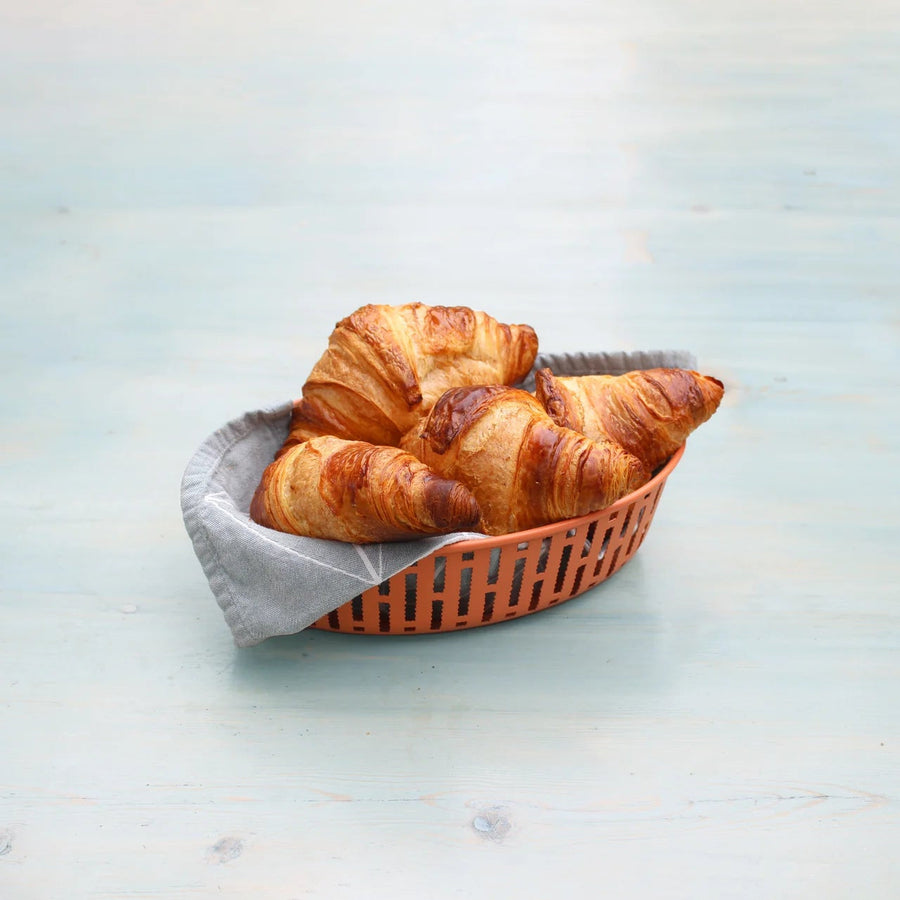 Three croissants in a brown basket on a light blue surface