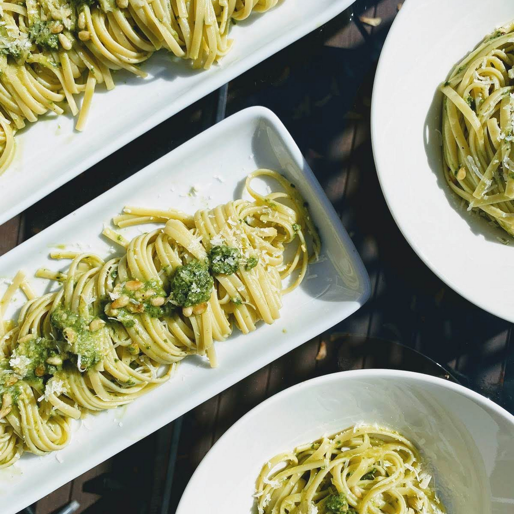 Overhead view of linguine tossed in green pesto with pine nuts and grated Parmesan on white plates.