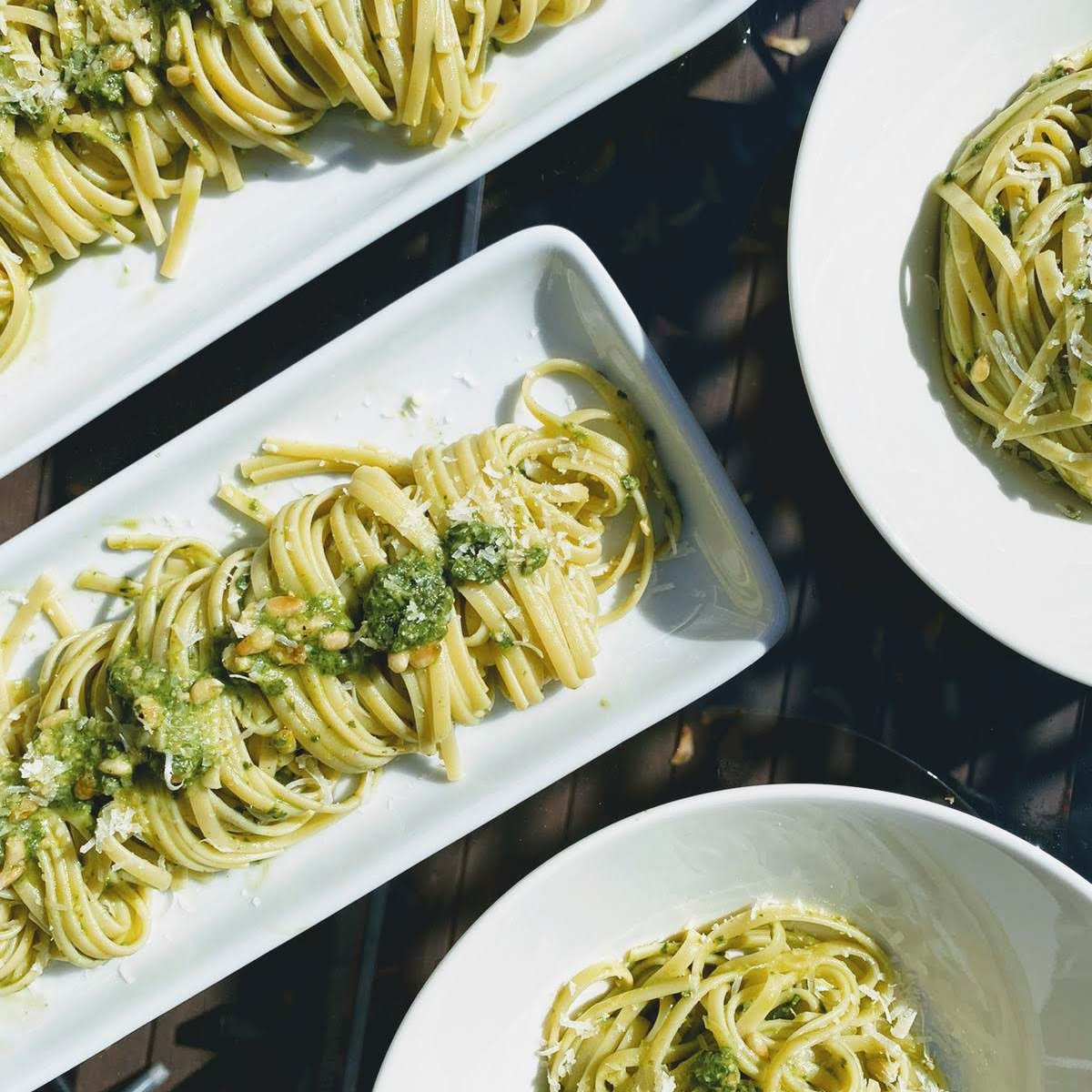 Overhead view of linguine tossed in green pesto with pine nuts and grated Parmesan on white plates.