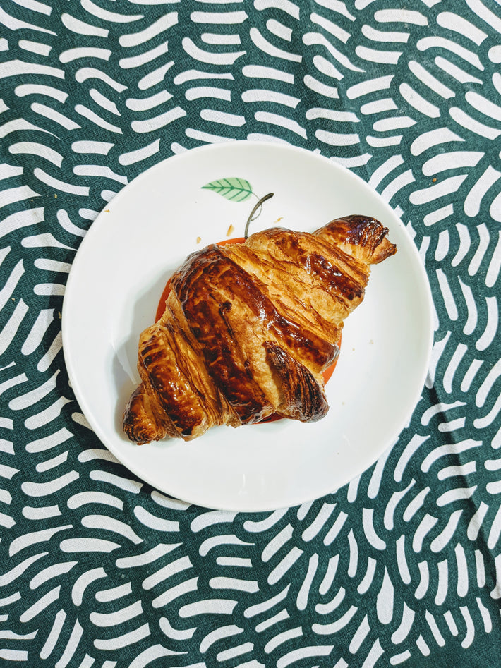 A flaky croissant on a white plate with a leaf design