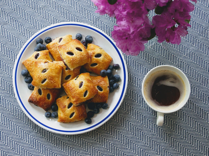 A plate of blueberry pastries with a cup of coffee and flowers in the background