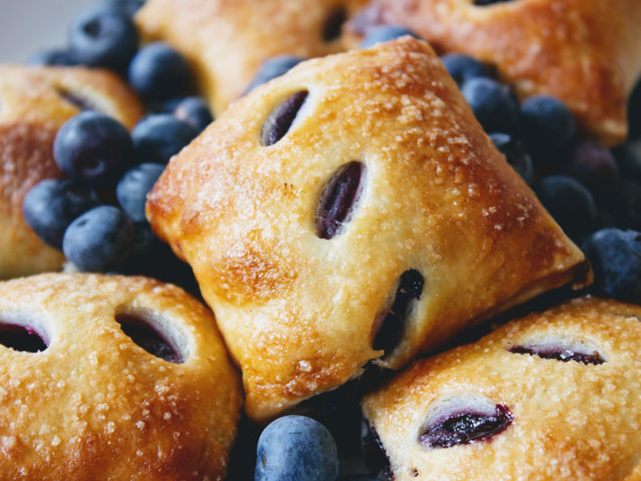 Golden-brown blueberry pie bites surrounded by fresh blueberries