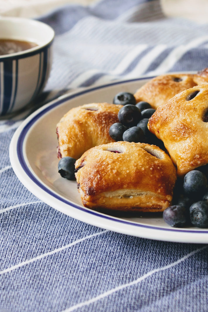Plate of blueberry pie bites with fresh blueberries and a cup of coffee in the background