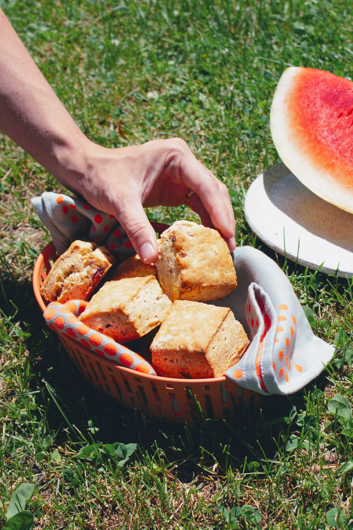 A hand holding orange-cranberry biscuits in a basket with a watermelon slice in the background.