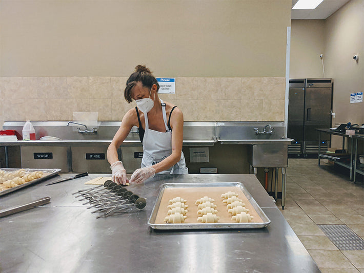 A person in a kitchen preparing croissants on a tray.