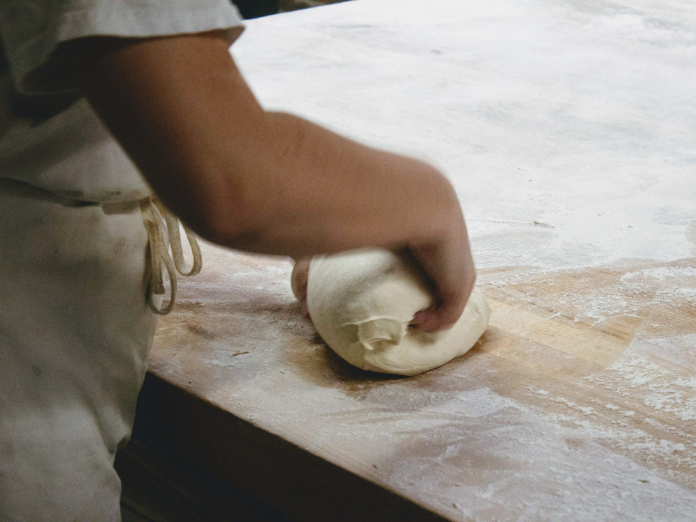 A person kneading dough on a wooden surface