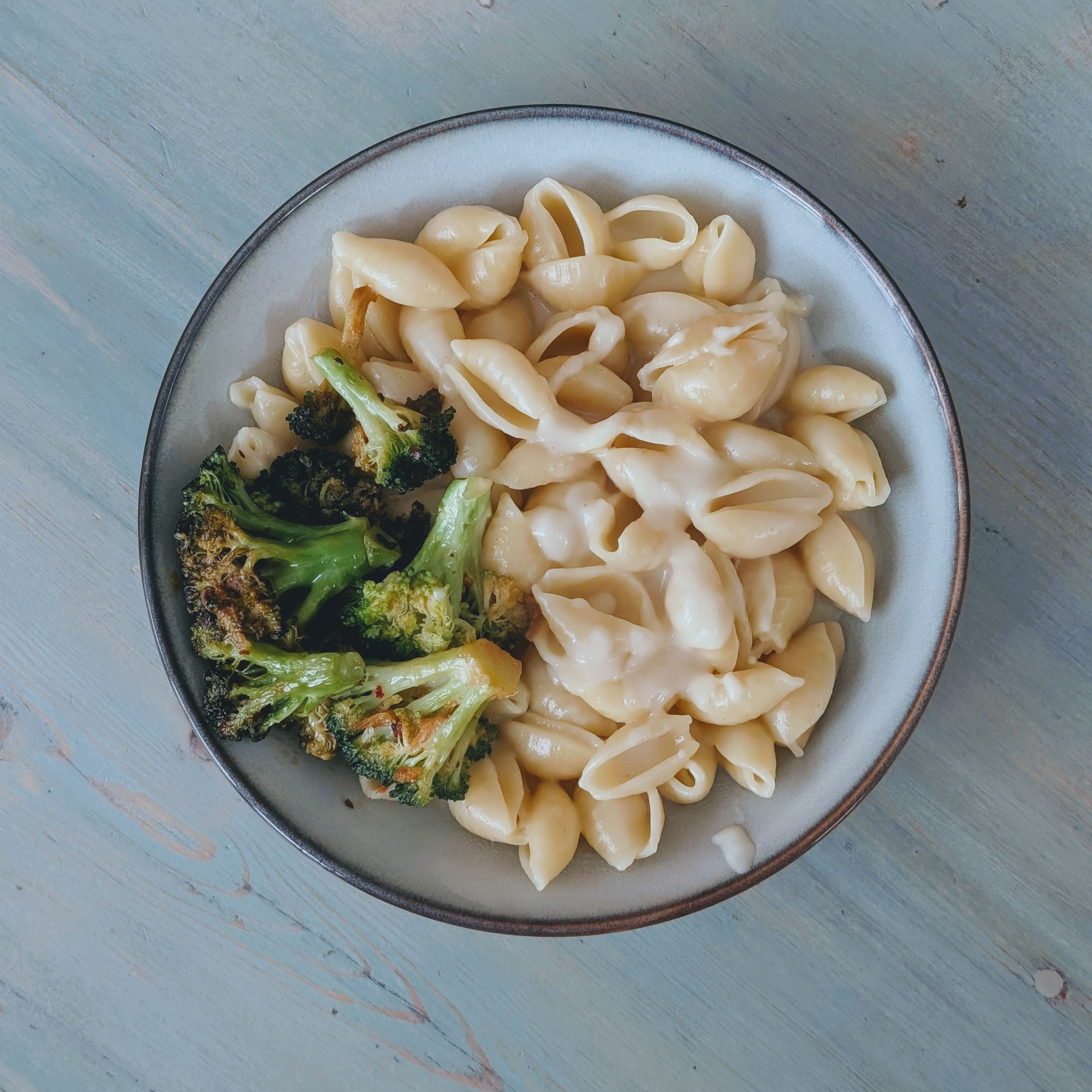 Top-down view of gluten-free mac and cheese with creamy cheese sauce and roasted broccoli in pale bowl on a light wood table
