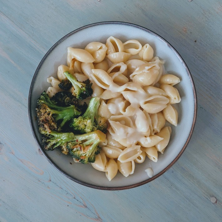 Top-down view of gluten-free mac and cheese with creamy cheese sauce and roasted broccoli in pale bowl on a light wood table