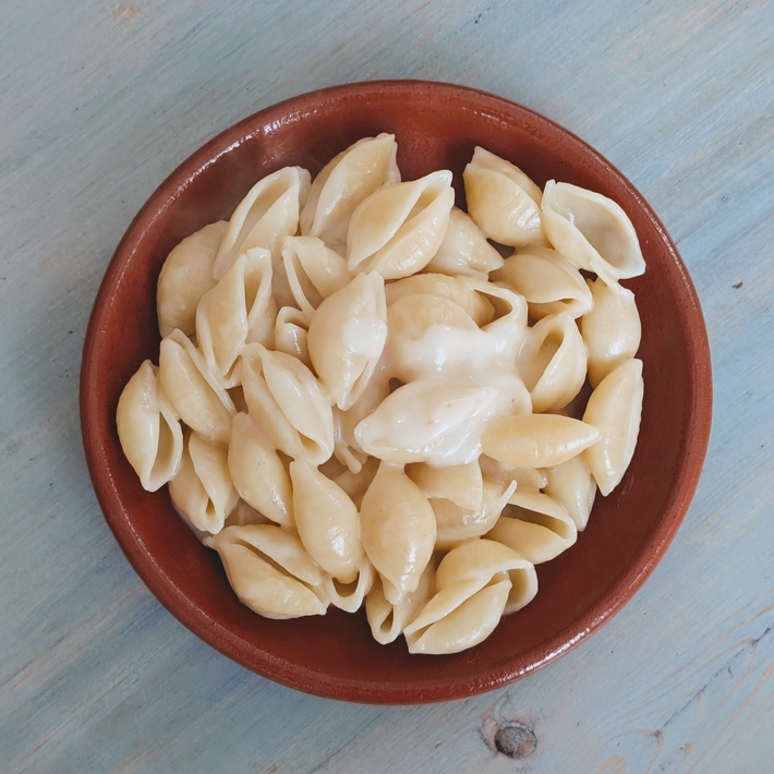 Top-down view of gluten-free shell pasta with creamy three-cheese sauce in a brown bowl on a pale blue wooden table