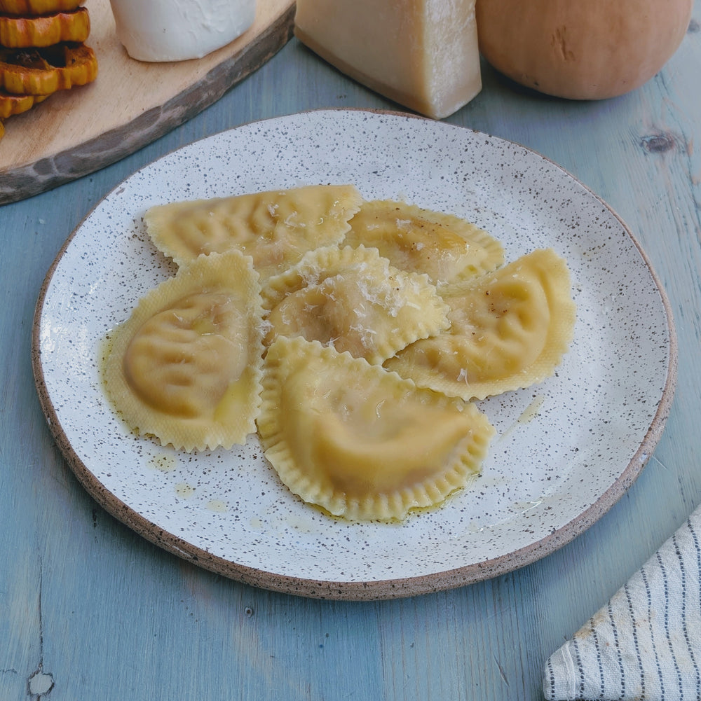 Butternut Squash & Cheese Ravioli on a plate with grated cheese, surrounded by cheese blocks.