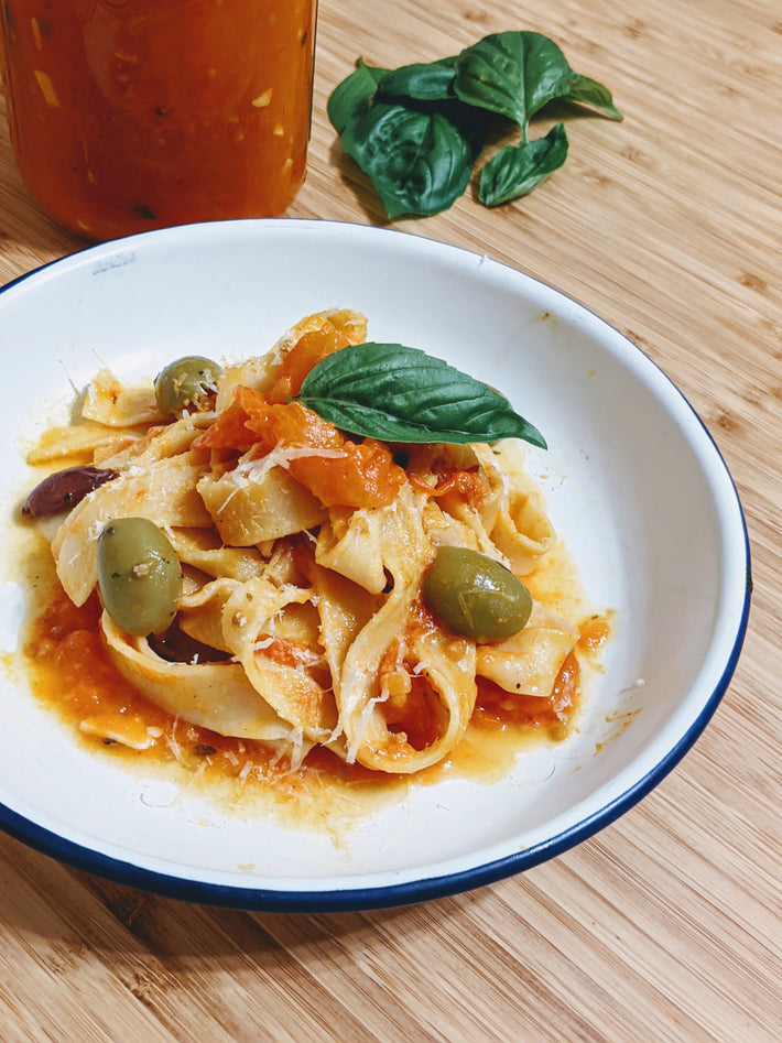 Pappardelle pasta with tomato sauce, olives, and basil in a bowl