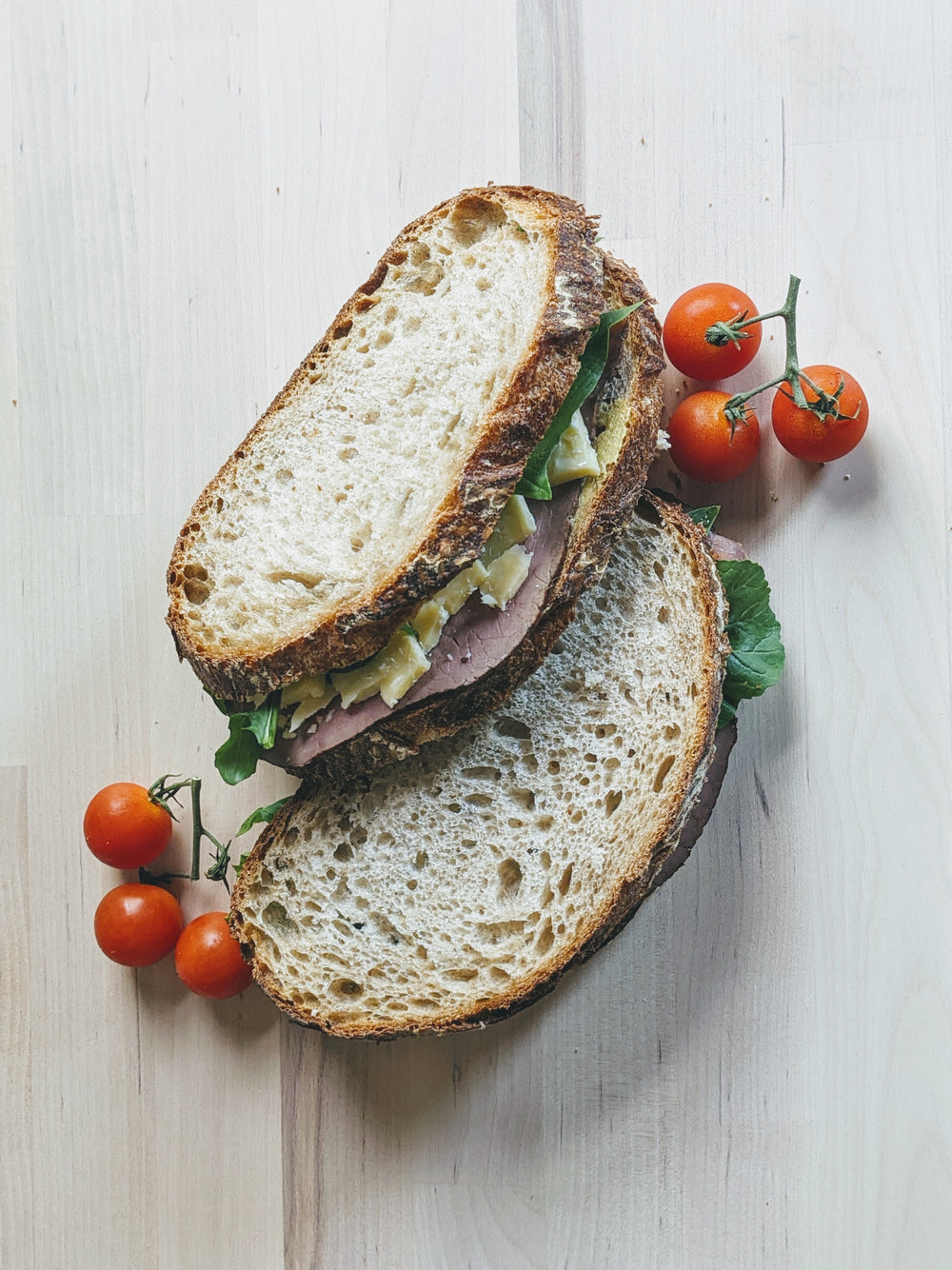 A sandwich made with sourdough bread, filled with greens and meat, served with cherry tomatoes.
