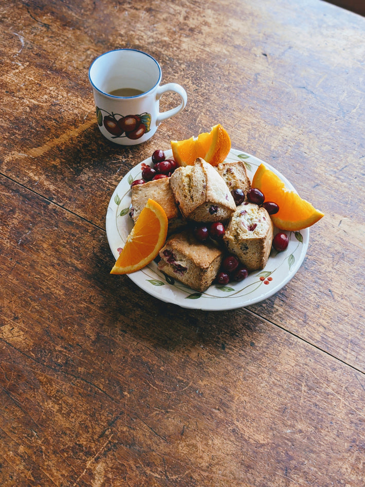 Orange cranberry biscuits on a plate with orange slices and a cup of coffee