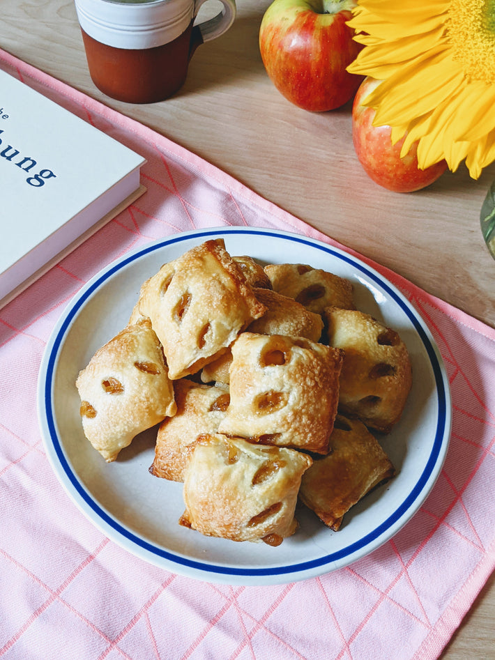 A plate of baked apple pie bites on a pink tablecloth with apples and a sunflower in the background.
