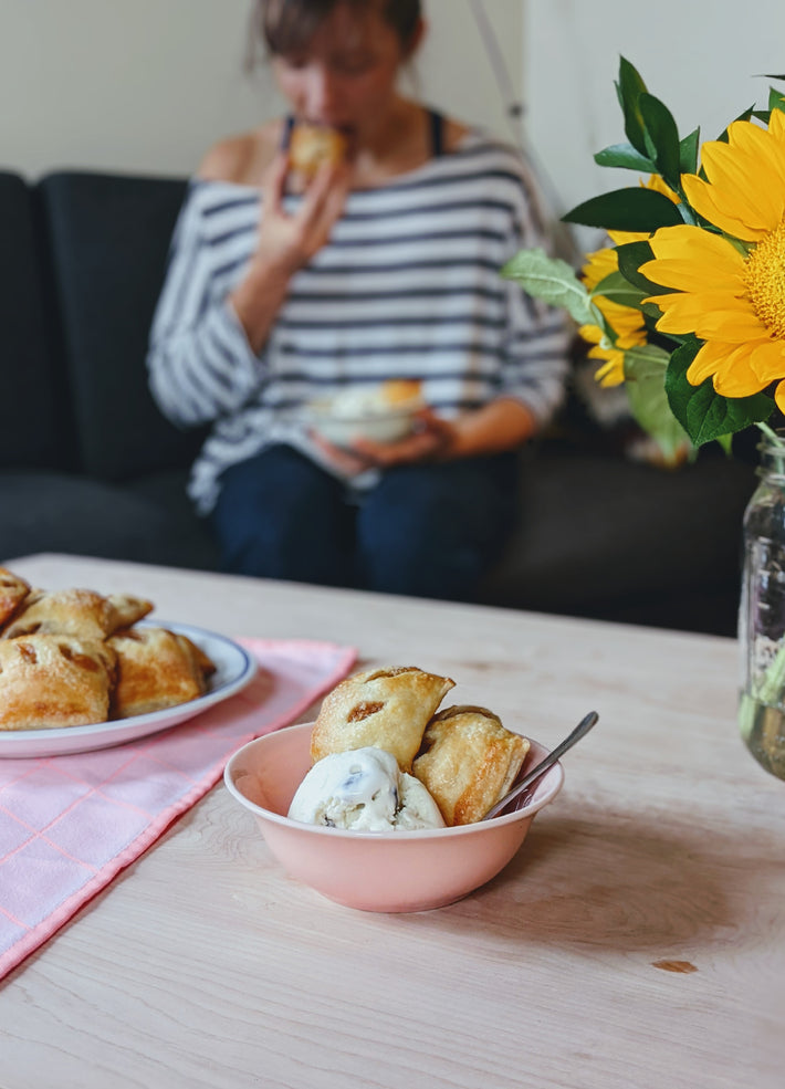 A person enjoying Wildgrain Apple Pie Bites with ice cream on a table with flowers
