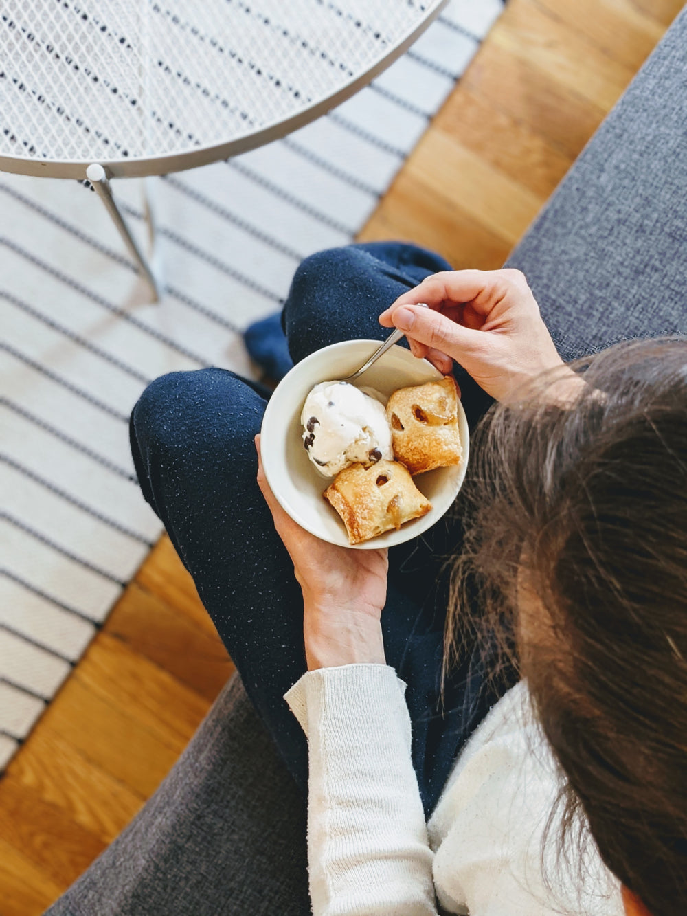 A person holding a bowl of dessert with frozen yogurt and pastry bites on a couch