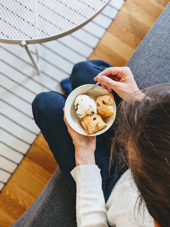 A person holding a bowl of dessert with frozen yogurt and pastry bites on a couch