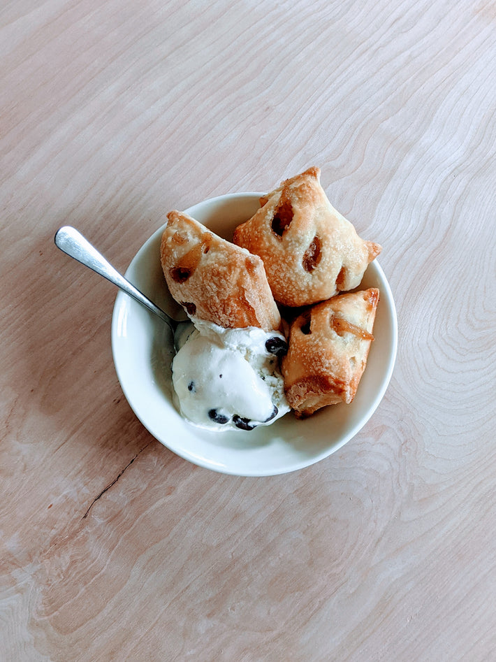 Three apple pie bites served with a scoop of vanilla ice cream in a bowl.