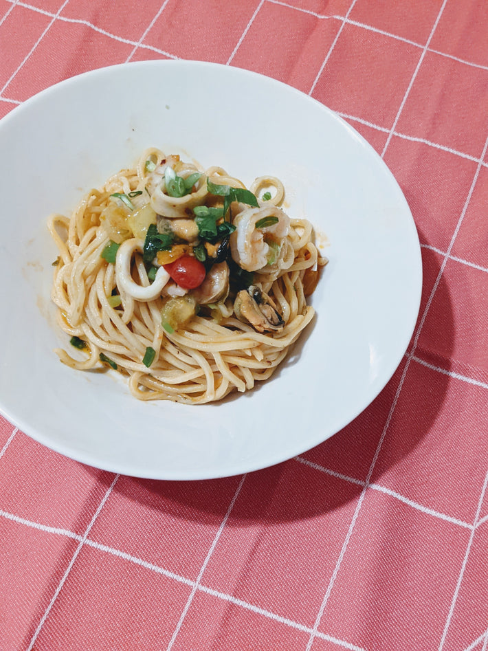Tonnarelli pasta with squid rings, mussels and cherry tomato in a white bowl on a pink checkered tablecloth