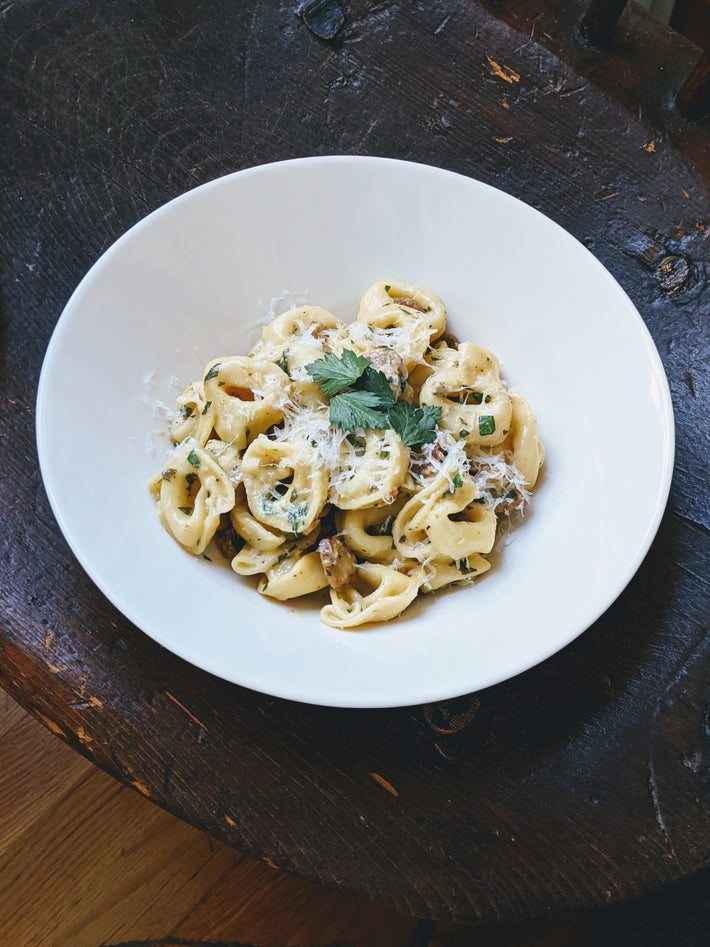 Cheese tortellini topped with herbs and cheese in a white bowl