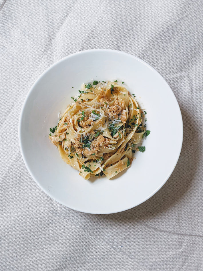 Plate of fresh fettuccine pasta topped with grated cheese and chopped herbs on a white tablecloth