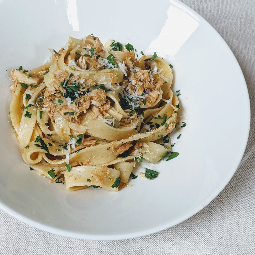 A bowl of pappardelle pasta topped with herbs and cheese