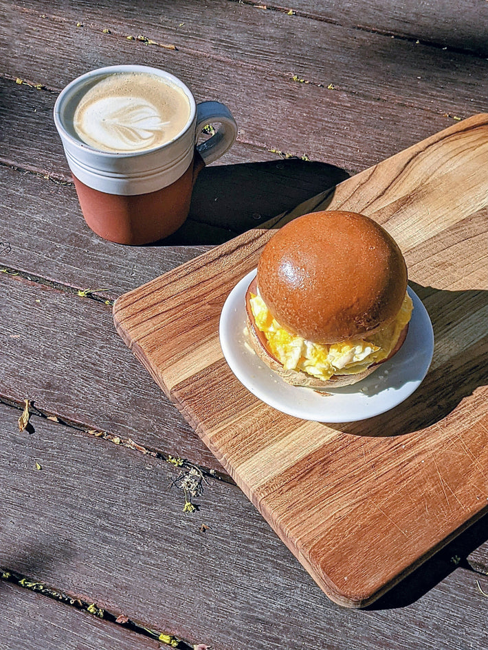 A cup of coffee and a slow-fermented brioche roll on a wooden board
